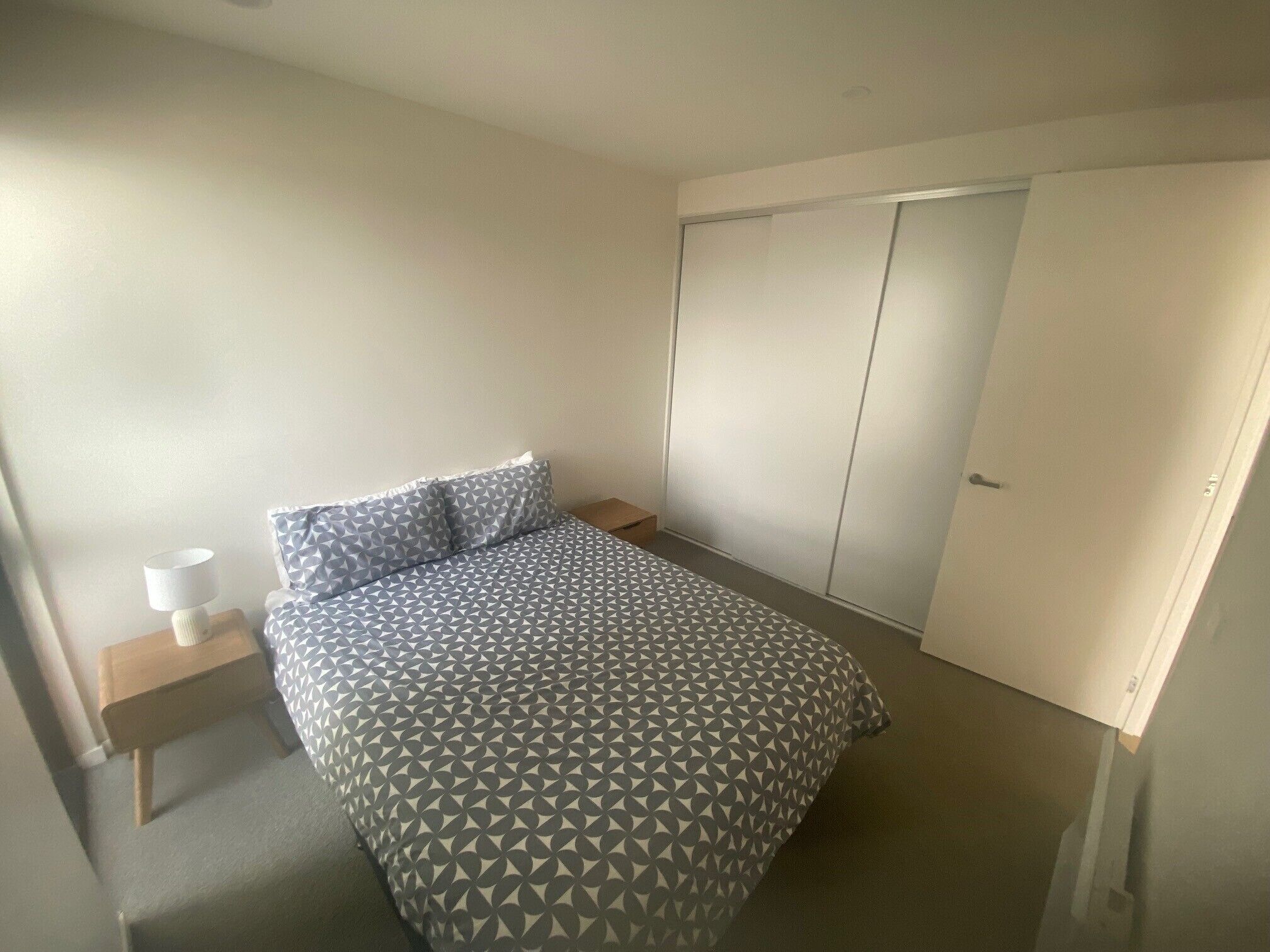 A bedroom with a bed, a nightstand, a wardrobe, and a door.
