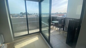 Een balkon met een glazen deur, een tafeltje met stoelen en uitzicht op de stad.