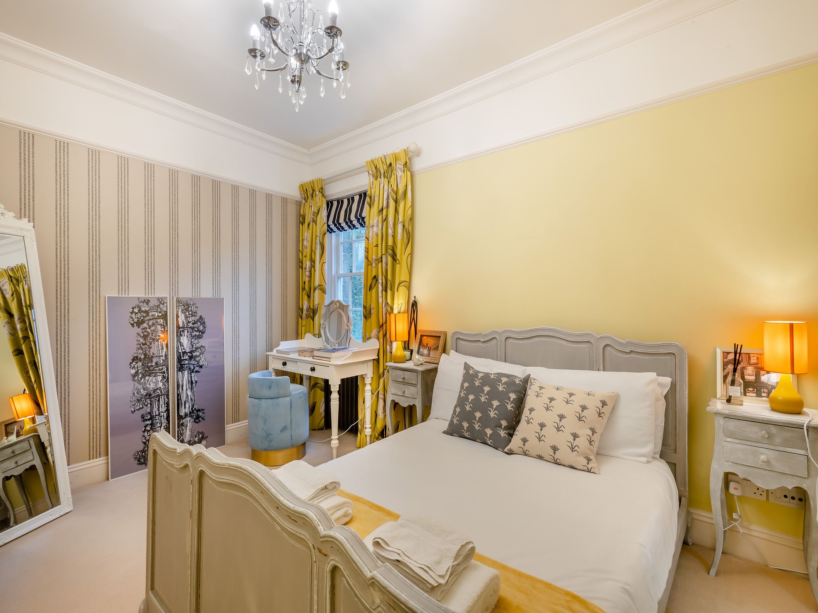 Une chambre bien aménagée, dotée d’un grand lit, d’une coiffeuse avec un miroir et d’un bureau avec une lampe.