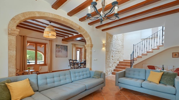 A spacious living area with a large light blue sofa, a smaller sofa, and a staircase leading to an upper floor.