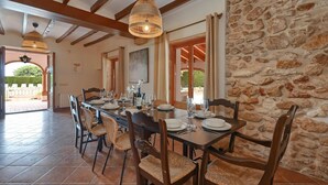 A dining area with a stone wall, wooden beams, and wicker chairs.