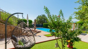 A pool area with a swing chair, lounge chairs, and a view of the pool.