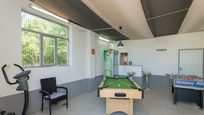 A room with a pool table, a foosball table, a treadmill, and a chair.