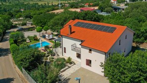 Una casa de dos pisos con techo de tejas rojas, piscina y paneles solares.