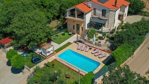 Une maison à deux étages avec une piscine, un espace salon extérieur et un jardin.