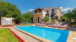 A pool with lounge chairs, a wooden deck, and a two-story building with a balcony. - Villa Ema - Makarska by Villas Guide (Donji Vinjani)