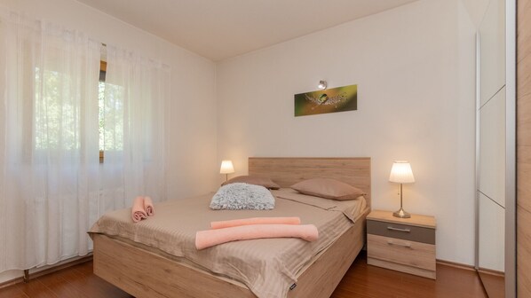 A bedroom with a wooden bed, two bedside lamps, a nightstand, and a window with sheer curtains.
