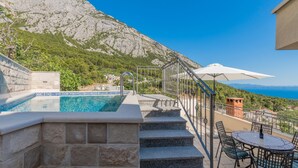 A pool with clear blue water, stone steps leading up to it, a white umbrella, and a view of a mountainous landscape. - Villa Ana - Makarska by Villas Guide (Makarska)