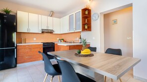 Een moderne keuken met een eetgedeelte, met een koelkast, oven en een houten tafel met stoelen.