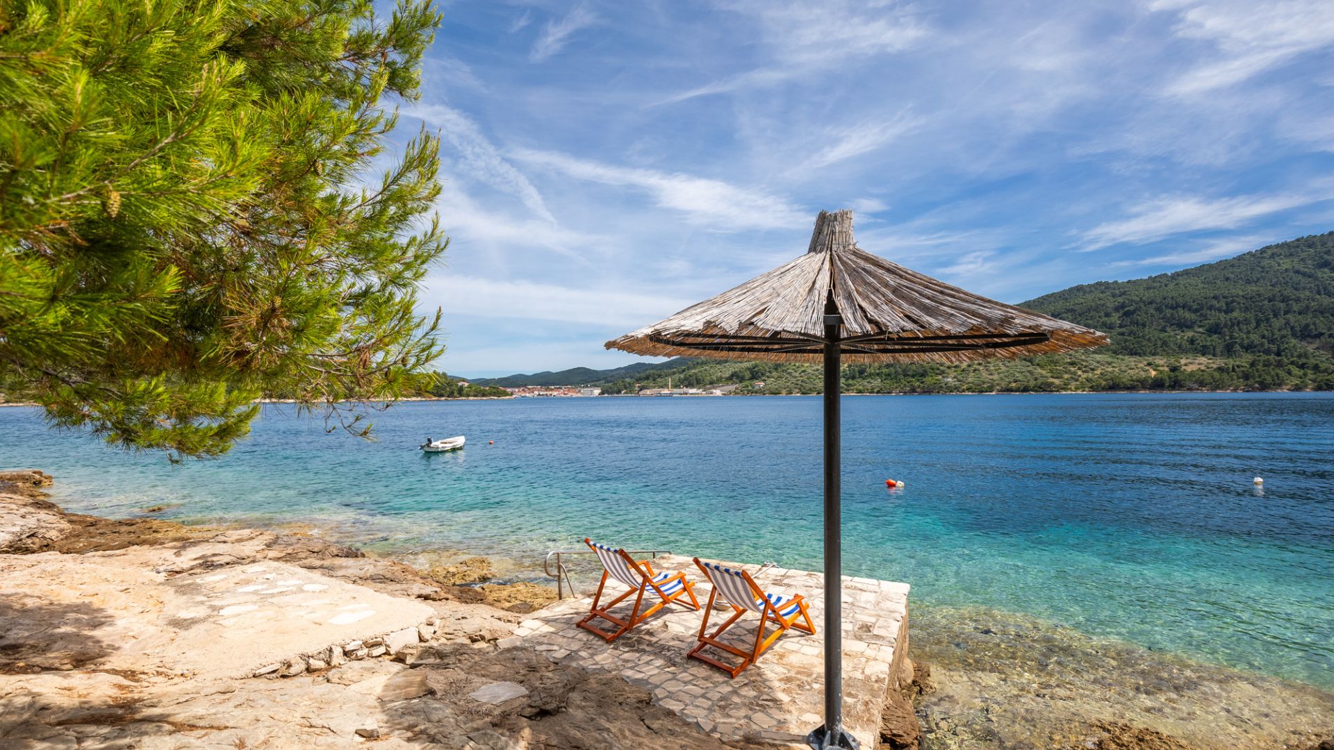A beach with clear water, a wooden umbrella, and two striped beach chairs.