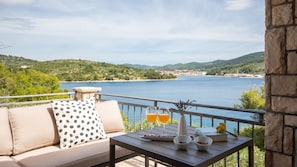 A balcony with a sofa, two glasses of orange juice, and a small table with bowls and a book. - Holiday home Erika by Villas Guide (Vela Luka)