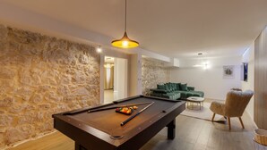 A pool table in a room with stone walls, a green sofa, and a fluffy chair.