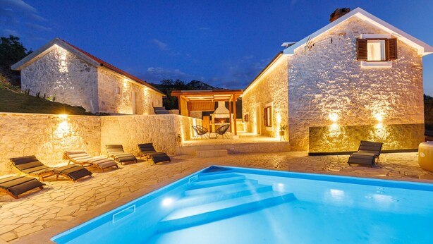 A stone villa with a swimming pool, outdoor seating, and a barbecue area.