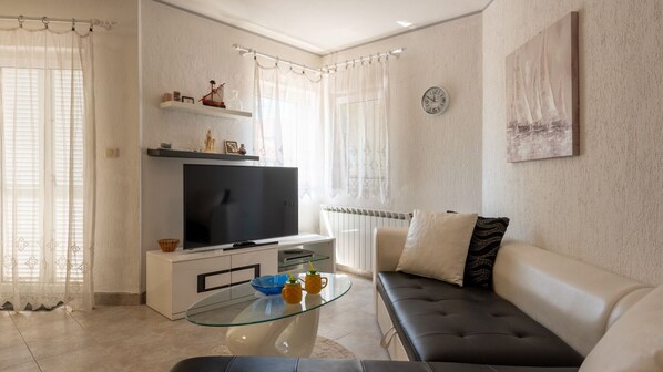 Un soggiorno con televisore, divano, tavolino in vetro e oggetti decorativi.