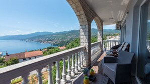 Un balcon offrant une vue sur un lac et des montagnes, avec un espace salon comprenant une table et des chaises.