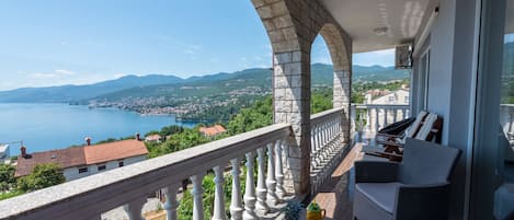 A balcony with a view of a lake and mountains, featuring a seating area with a table and chairs.