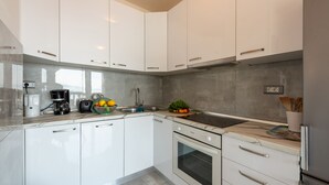 Une cuisine moderne avec des meubles blancs, un four encastré, une machine à café et un panier à fruits.
