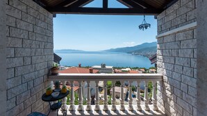 A balcony with a stone wall, a hanging light fixture, and a view of a lake and distant mountains. - Apartman Max 3 by Villas Guide (Rijeka)