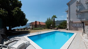 A swimming pool with lounge chairs, a stone building, and a view of the sea. - Apartman Max 3 by Villas Guide (Rijeka)