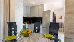 A modern kitchen with white cabinets, a glass dining table with chairs, and a fruit bowl. - Apartman Max 3 by Villas Guide (Rijeka)