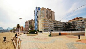 A beachfront hotel with multiple floors, balconies, and a sandy beach area in the foreground.