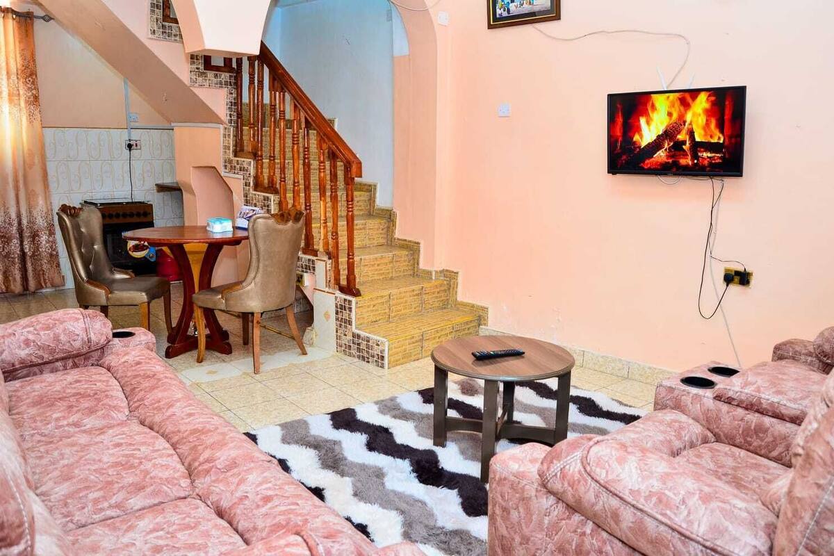 Un salon avec un escalier, un coin repas et un téléviseur diffusant une image de feu de cheminée.