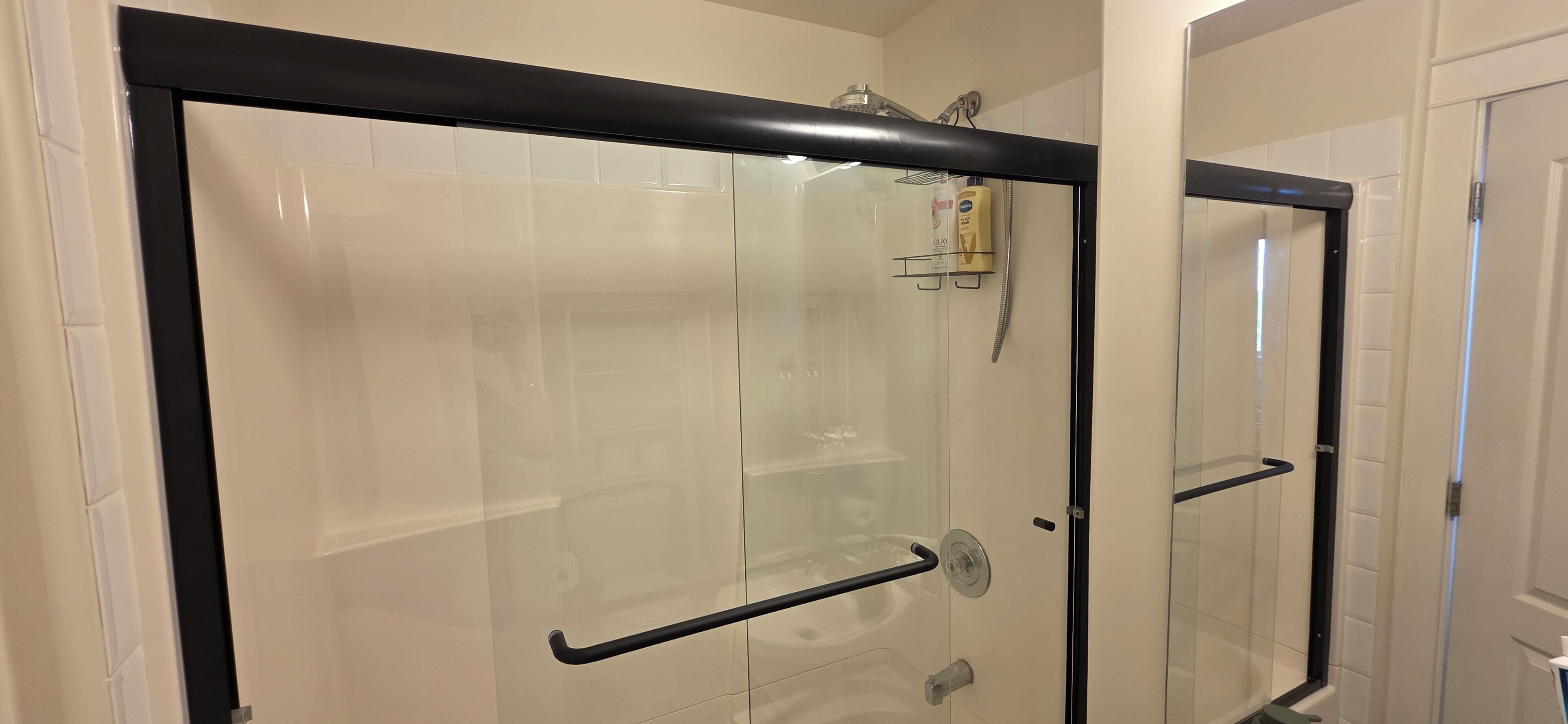 Una cabina doccia in vetro con cornice nera, porta in vetro e soffione a parete.
