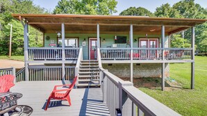 Eine zweistöckige Holzhütte mit überdachter Veranda, Feuerstelle und Gartenmöbeln.