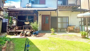 A residential building with a covered patio, a front door, and a small garden area. - Tsukiyama Inn (Yamatotakada)