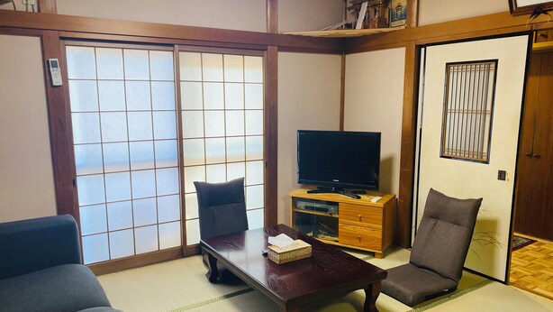 A traditional Japanese-style living room with tatami flooring, a television on a wooden stand, and a sliding door with a grid pattern. - Tsukiyama Inn (Yamatotakada)