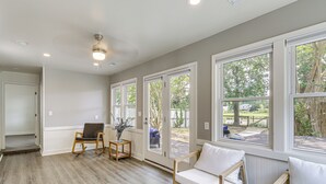 A spacious room with hardwood flooring, a white sofa, a rocking chair, and large windows offering a view of the outdoors. - Riverfront Fun: Quiet Home Near Hampton Coastline (Hampton)