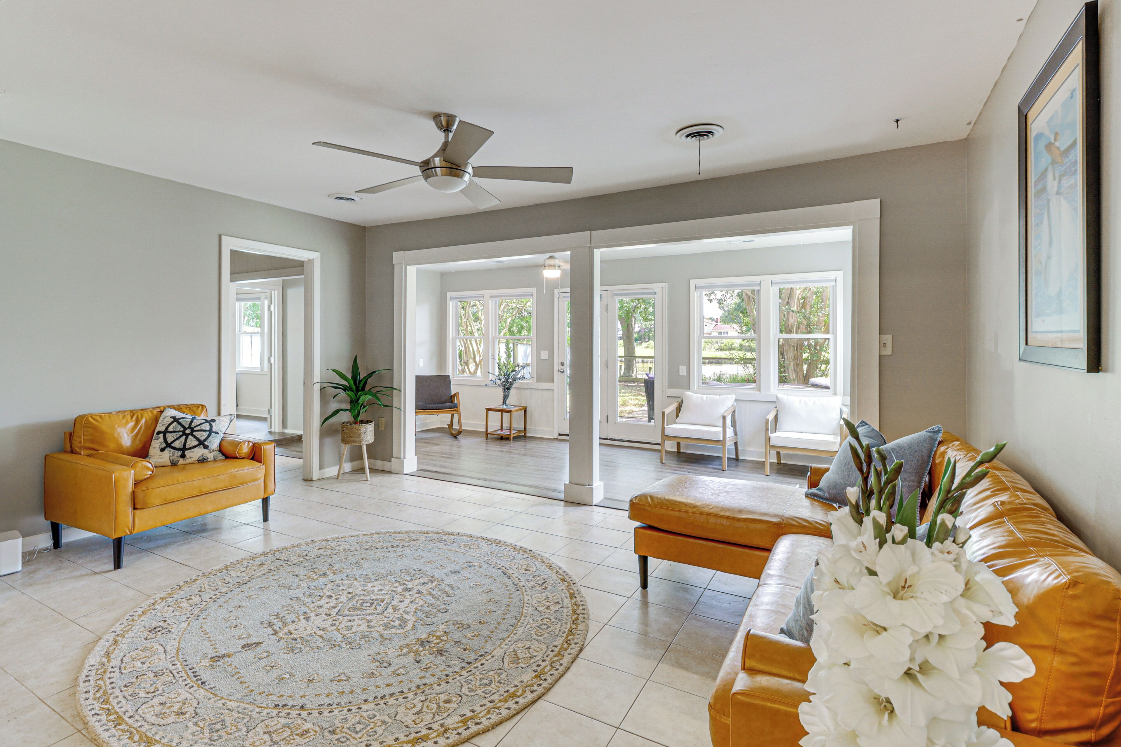 A spacious living room with a yellow sofa, a round rug, and a ceiling fan.