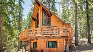Een houten chalet met een balkon, omgeven door hoge bomen.