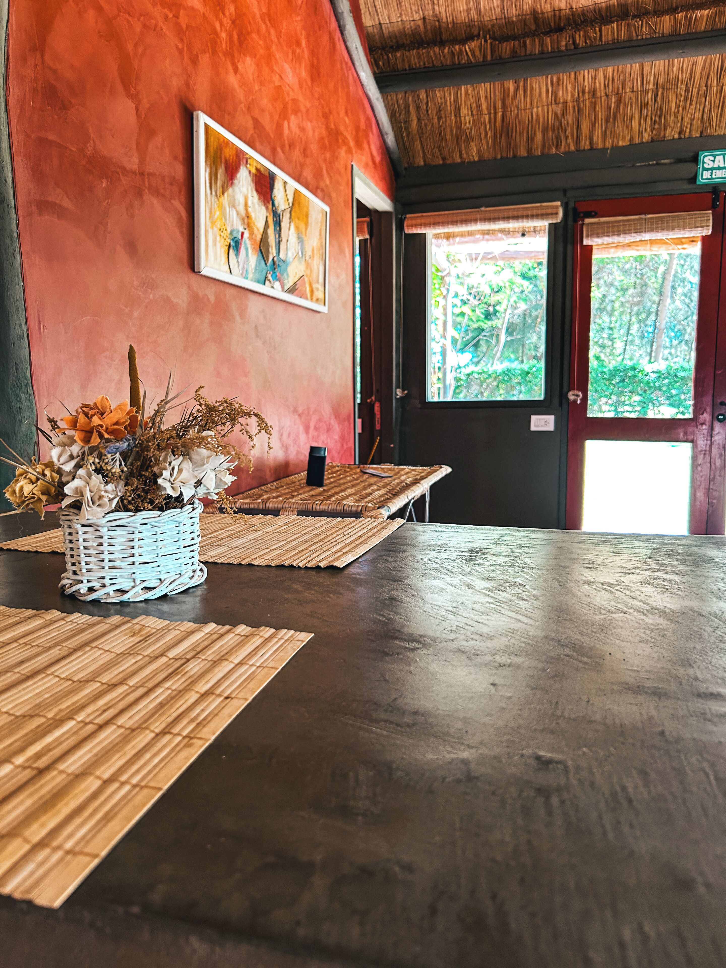 A room with a dark wooden floor, a woven mat, a wicker basket with dried flowers, and a painting on the wall.