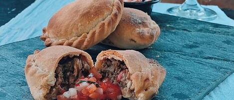 A table with a plate of stuffed pastries and a glass of red wine, set against a brick oven with a fire.