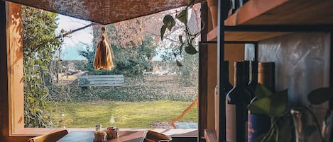 Un comedor con una mesa y sillas, vista a un jardín y una estantería con botellas de vino.