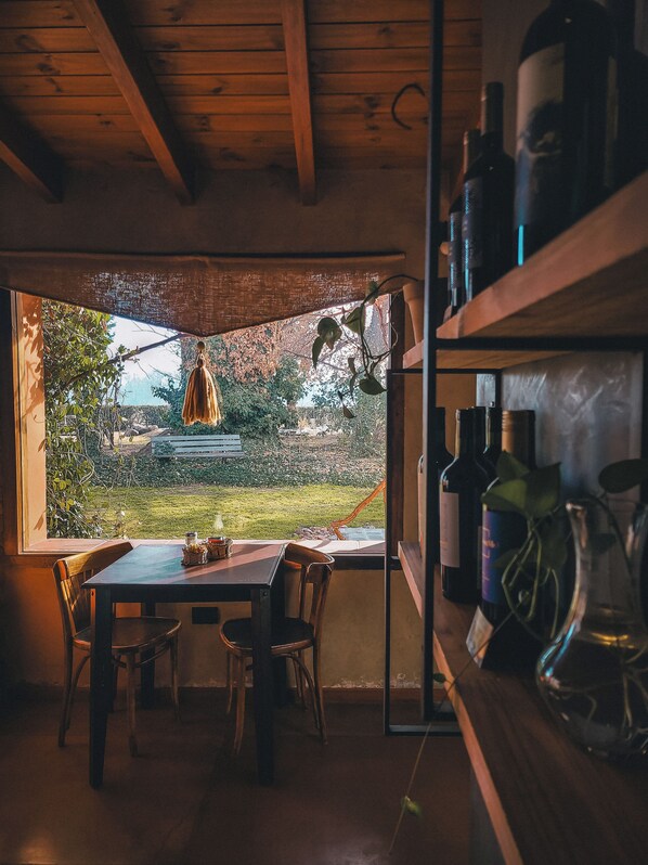 Un comedor con una mesa y sillas, vista a un jardín y una estantería con botellas de vino.