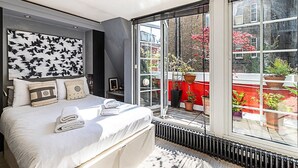 A modern bedroom with a large bed, a view of the city through a sliding glass door, and a cityscape visible through the window.