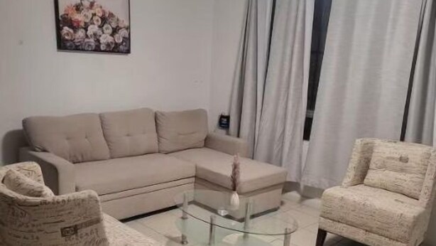Un salon avec un canapé beige, deux fauteuils à motifs, une table basse en verre et un tableau accroché au mur.