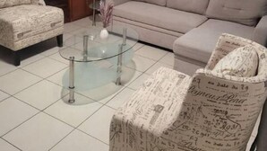 Un salon comprenant un canapé, des fauteuils, une table basse en verre et un escalier.