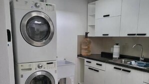 Une cuisine compacte équipée d’un lave-linge et d’un sèche-linge intégrés, d’un évier et de meubles de rangement blancs.