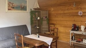 Une pièce chaleureuse avec un plafond en bois, une table à manger avec des chaises, un canapé, un petit meuble et un tableau accroché au mur.