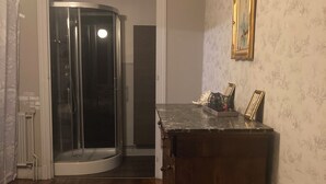 Une pièce avec un plancher en bois, une cabine de douche en verre, un meuble en bois foncé et un papier peint à motifs.