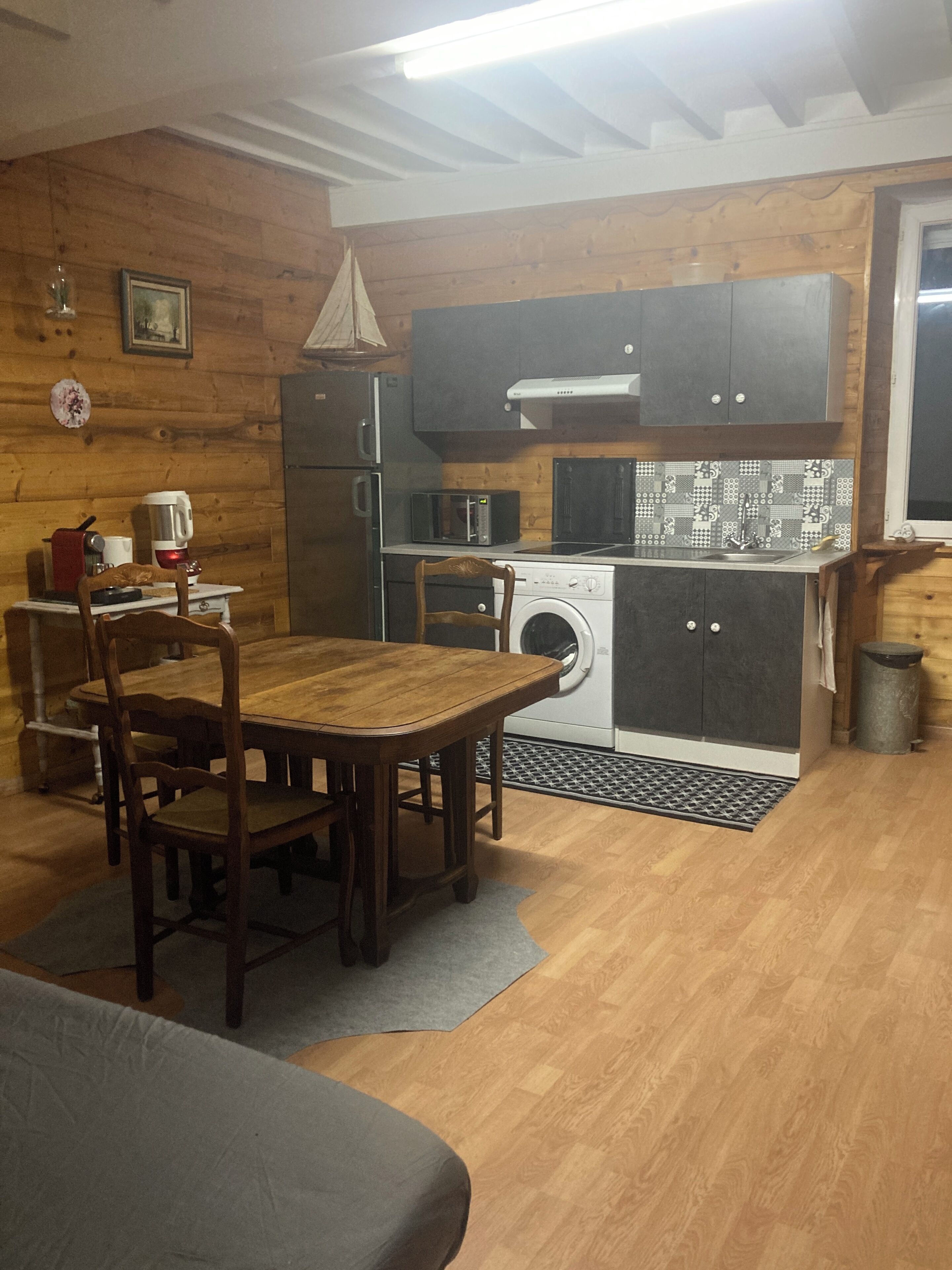 Een compacte keuken met houten kastjes, een wasmachine, een magnetron, en een eethoek met een tafel en stoelen.