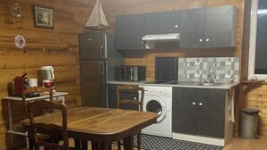 Une cuisine compacte dotée de meubles en bois, d’un lave-linge, d’un four à micro-ondes et d’un coin repas avec une table et des chaises.