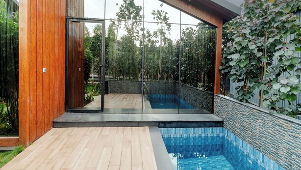 Una casa moderna con piscina, terraza de madera y puertas de cristal que dan a un patio.
