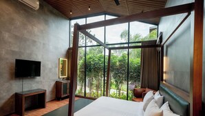 A modern bedroom with a large bed, a TV, and a view of greenery through large windows. - Forrest (Mahabalipuram)