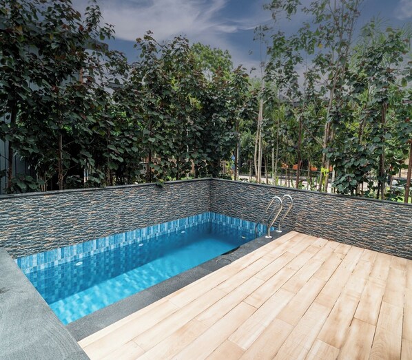 A swimming pool with a stone border, surrounded by a wooden deck and trees. - Forrest (Mahabalipuram)