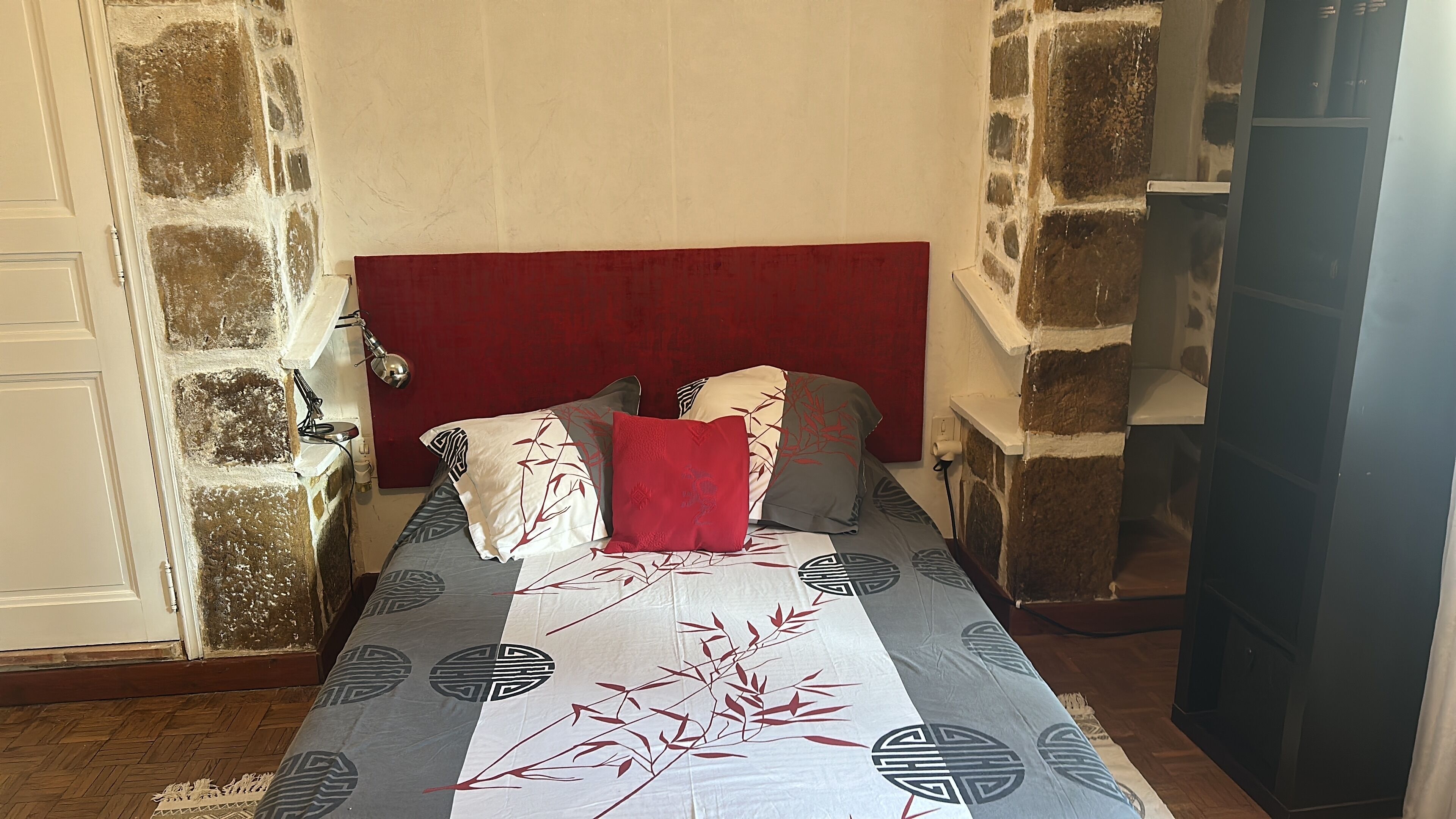 Una cama con ropa de cama estampada, un cabecero rojo y una pared de piedra.