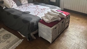 Un dormitorio con pared de piedra, cama con ropa de cama estampada, mesita de noche, ventana con vistas a zonas verdes y suelo con patrón de espiga.